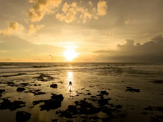 Un vibrante tramonto su una costa rocciosa dell'oceano. Il sole, un globo bianco brillante, si riflette sulla sabbia bagnata