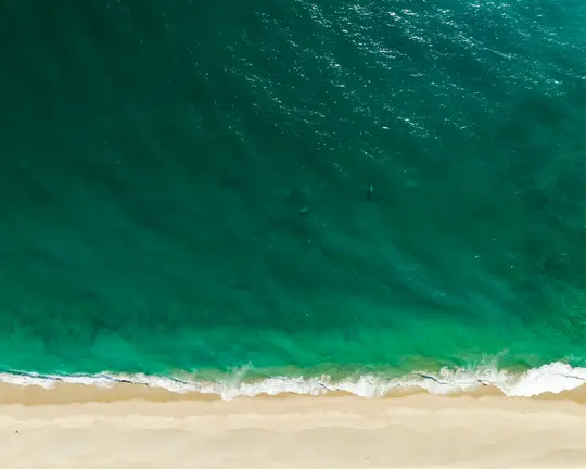 Uno scatto aereo che guarda dritto verso il basso su un'ampia spiaggia sabbiosa che incontra l'oceano turchese e verde acqua