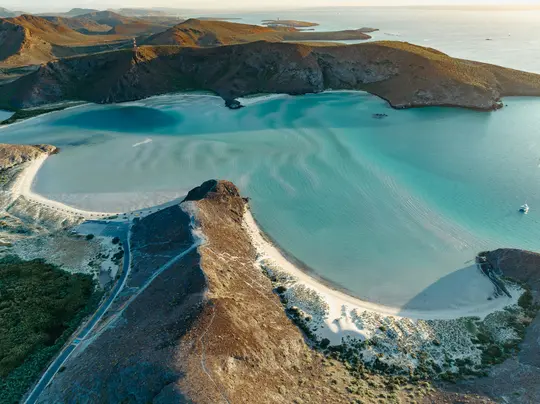 En luftvy fångar en fantastisk vik med klart turkost vatten, inramad av karga, bruna, torra kullar och en vit sandstrand.