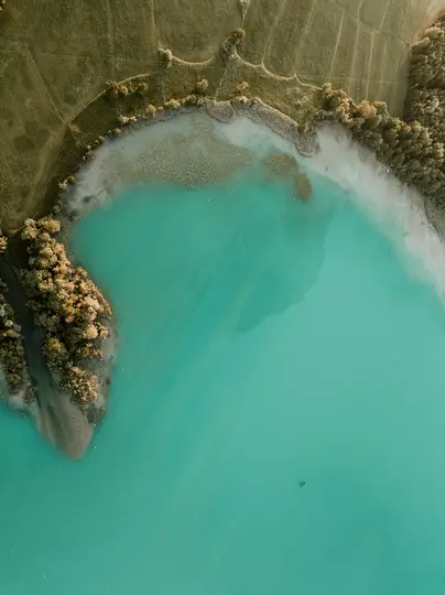 Una fotografia aerea cattura un lago turchese brillante con una piccola forma scura e indistinta al centro. Il lago è...
