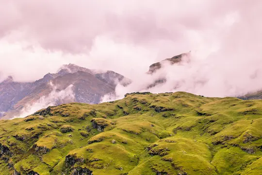 Un'ampia vista panoramica di lussureggianti colline verdi in primo piano, con montagne marroni e grigie frastagliate sullo