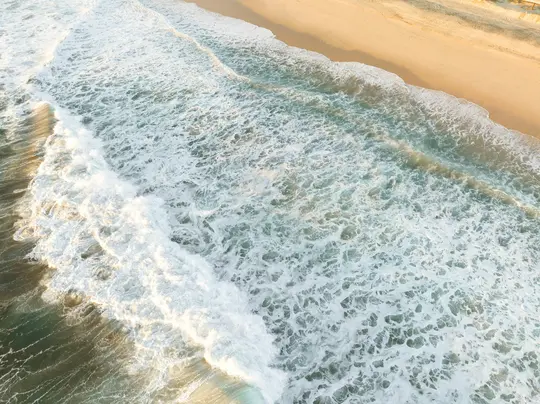 Una vista aerea cattura la schiuma bianca ritmica delle onde dell'oceano che si infrangono su una spiaggia sabbiosa color