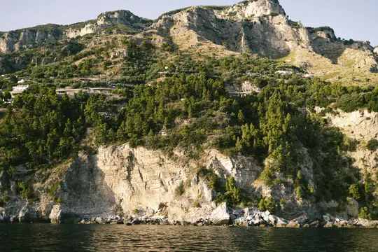 Un'ampia vista panoramica di una montagna aspra e coperta di alberi che si eleva ripidamente dal mare blu scuro sotto un