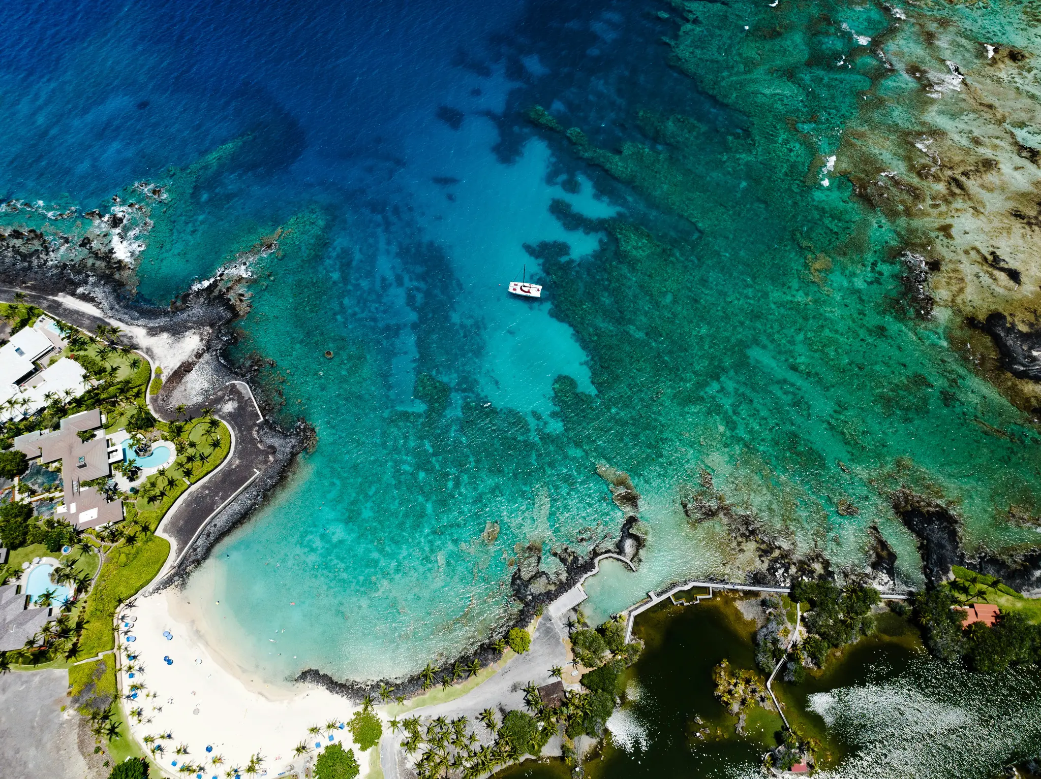 Une prise de vue aérienne d'une côte tropicale présente une plage de sable blanc, un océan bleu clair et turquoise, et des