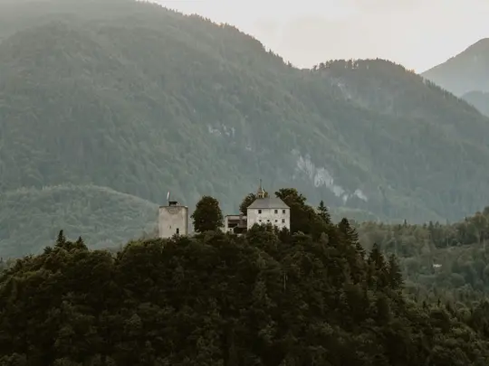 Un edificio bianco con tetto scuro e una torre in pietra con una bandiera rossa e bianca si erge su una collina