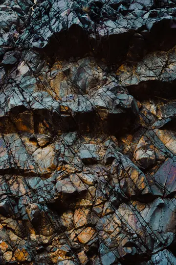 A detailed close-up of a rock face, showing a complex pattern of cracks and fissures in dark blue, gray, and orange tones.
