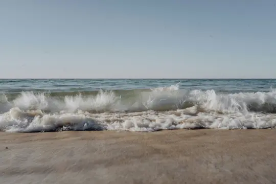 Una ripresa ampia di un'onda oceanica che si infrange su una spiaggia sabbiosa di colore marrone chiaro sotto un cielo