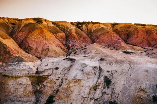 Un'ampia foto paesaggistica di colline erose che mostrano distinti strati di terra rossa, arancione, marrone e beige sotto un