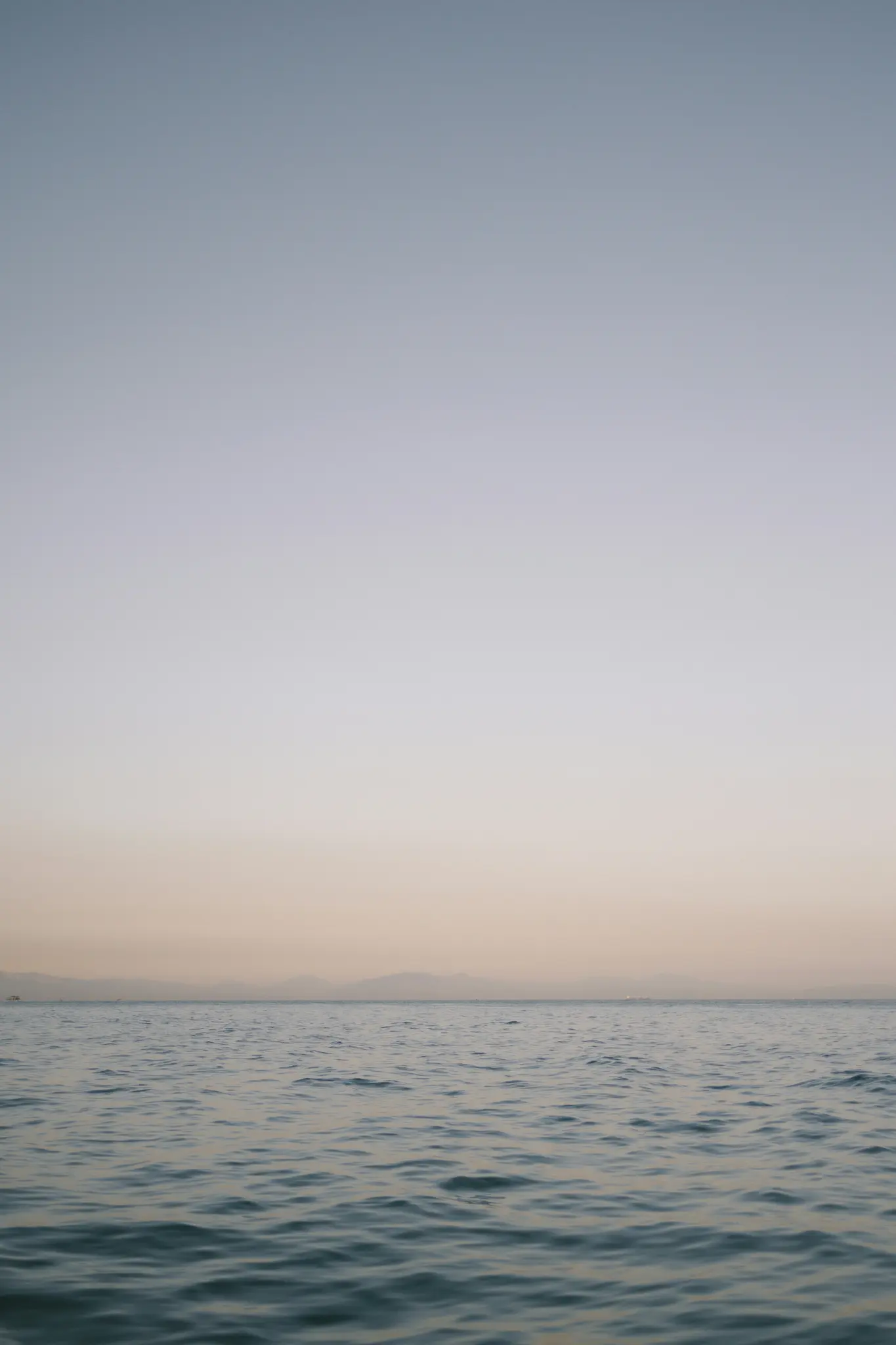 Ett minimalistiskt foto av en lugn ocean med mjuka krusningar, som möter en mjuk gradienthimmel som övergår från ljusblått