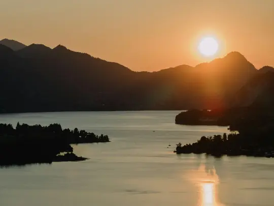 Ein lebendiger Sonnenuntergang über einem ruhigen See, die Sonne tief am Horizont wirft einen orangefarbenen Glanz auf das
