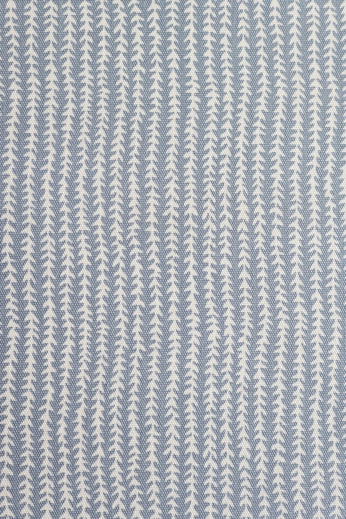 Gros plan d'un tissu présentant un motif répétitif de petites formes d'arbres stylisées blanches sur fond bleu clair.