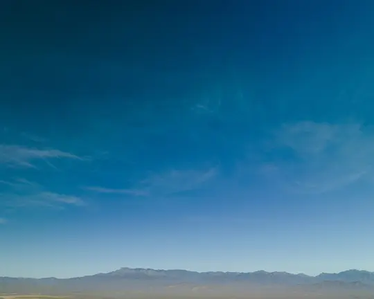 Un'ampia foto di paesaggio che mostra un cielo blu intenso con nuvole leggere e vaporose, che si estende su una catena
