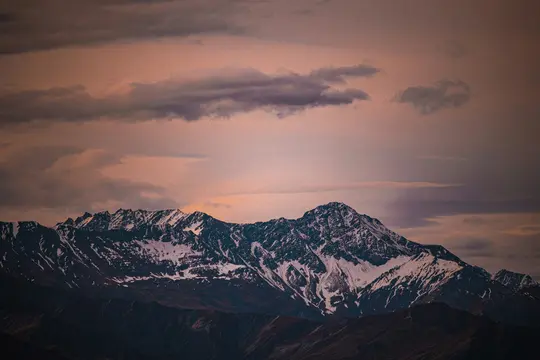 Ett brett landskapsfoto visar en karg bergskedja med snö på topparna och sluttningarna, under en himmel fylld av mörka moln.