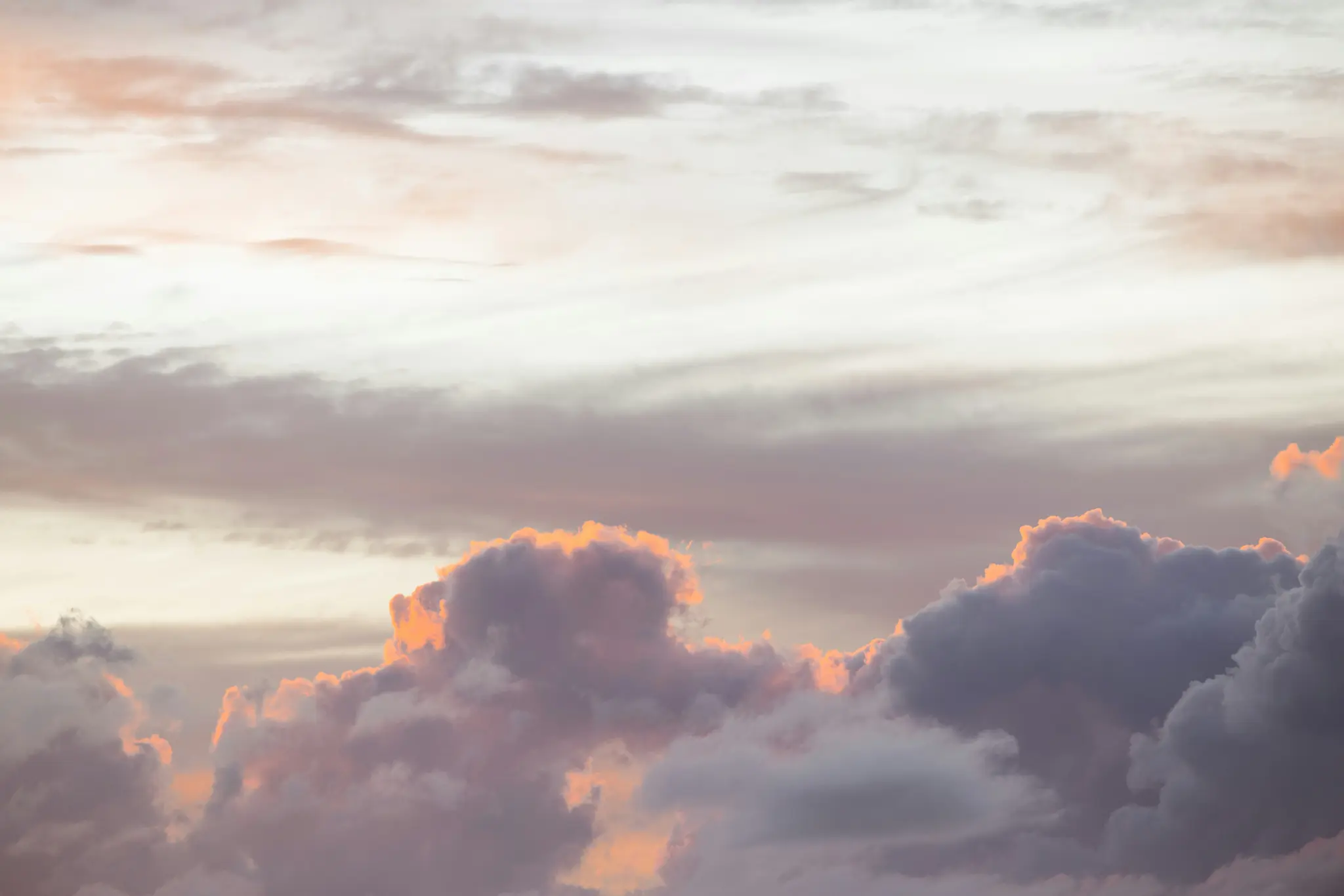 Eine Weitwinkelaufnahme eines wolkenverhangenen Himmels. Die unteren Wolken sind dunkelviolett und grau, ihre Spitzen werden