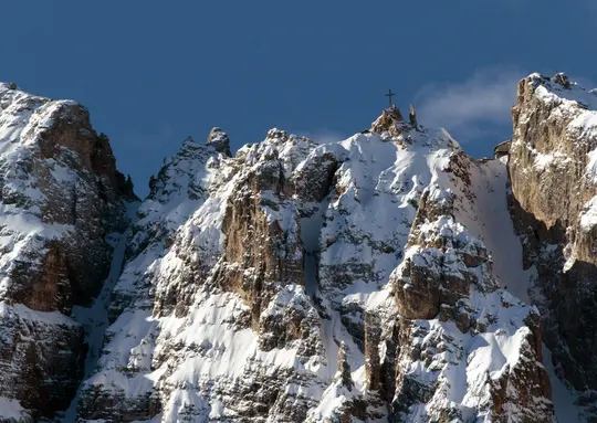 Eine majestätische Aussicht auf schneebedeckte Berggipfel unter einem klaren blauen Himmel, mit einem Kreuz auf einem Gipfel