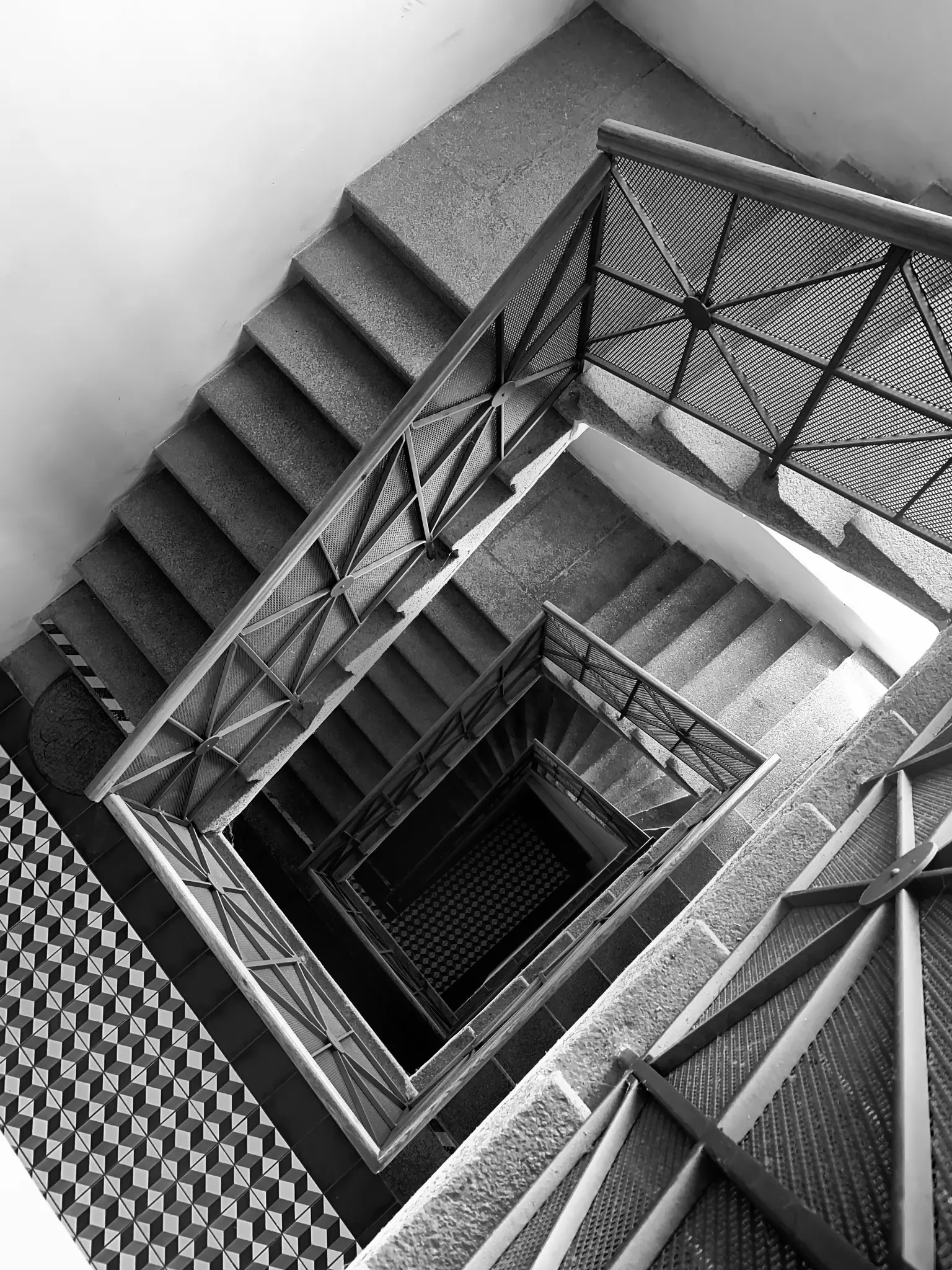 Hochwinkel-Schwarz-Weiß-Foto, das eine quadratische Wendeltreppe mit kunstvollen Metallgeländern zeigt.