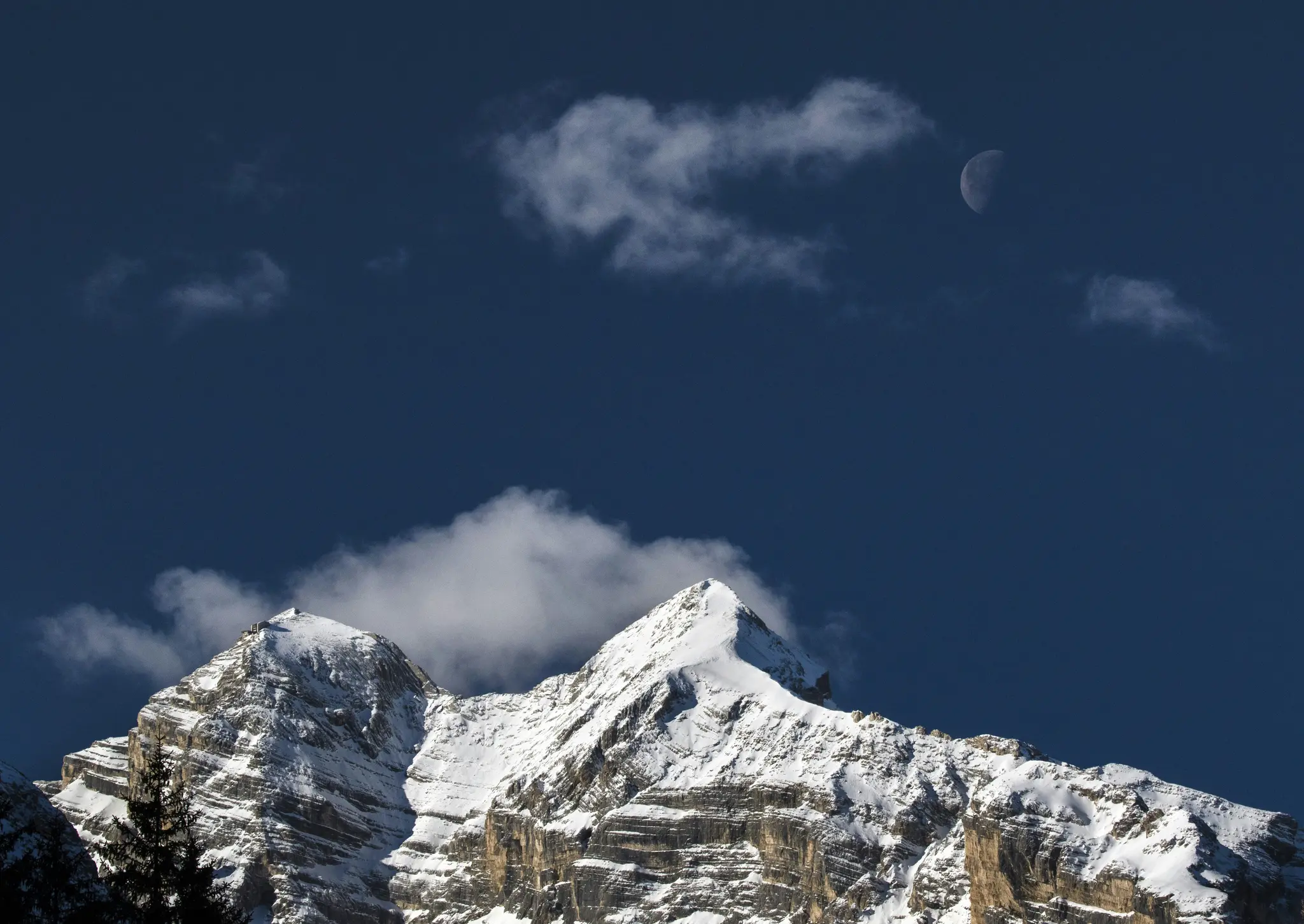 Ein majestätischer Blick auf schneebedeckte Berggipfel unter einem dunkelblauen Himmel. Eine Mondsichel ist oben rechts