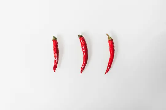 Three vibrant red chili peppers with green stems are arranged vertically and evenly spaced on a stark white background.