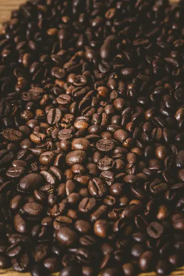 O fotografie foarte apropiată, cu vedere de sus, a numeroși boabe de cafea prăjite intens, umplând întregul cadru. Boabele