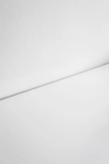 Et minimalistisk foto, der viser en tekstureret hvid væg, der møder en glat hvid overflade, adskilt af en tynd, let sløret