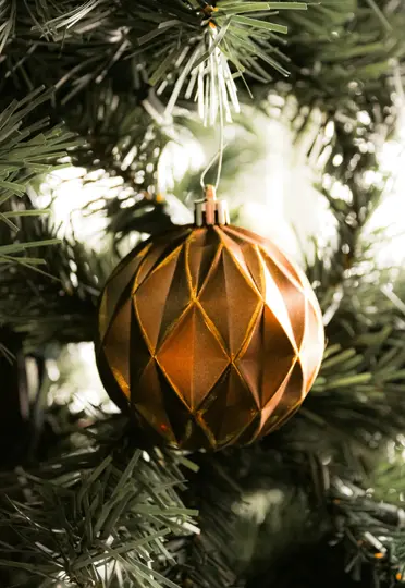 Et nærbillede af en gylden, facetteret julepynt, der hænger på de mørkegrønne nåle på et kunstigt juletræ.