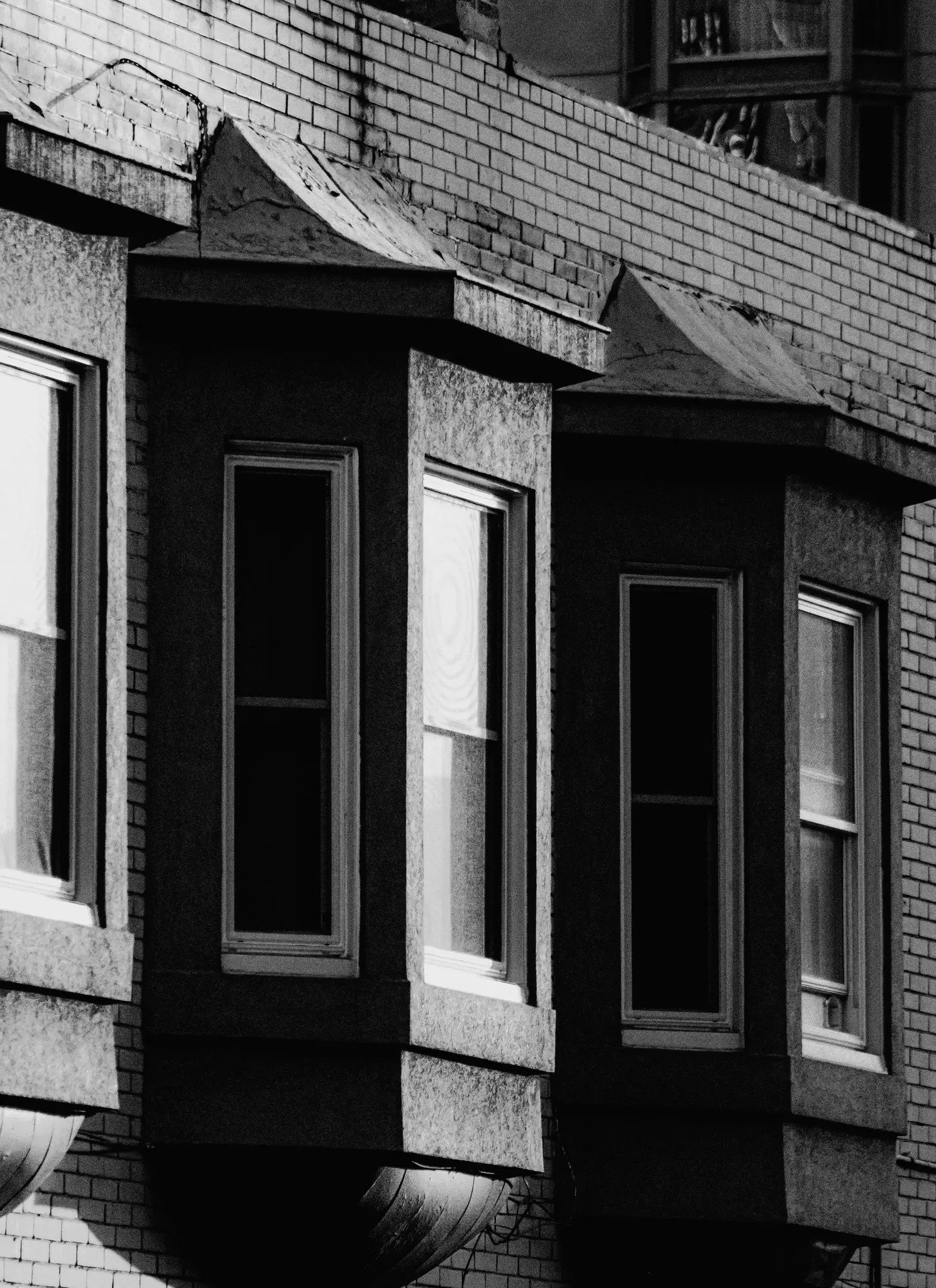 Černobílý detailní záběr ze spodního úhlu na tři arkýře na cihlové budově, ukazující architektonické detaily.