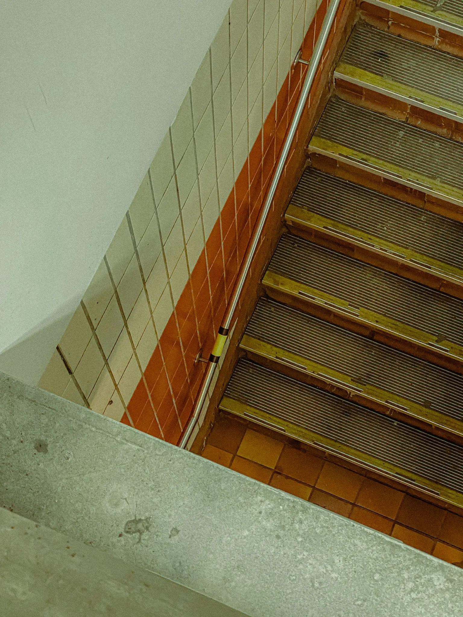 Záběr z výšky na dlážděné schodiště. Zeď vlevo je bílá svislým pruhem oranžových dlaždic. …