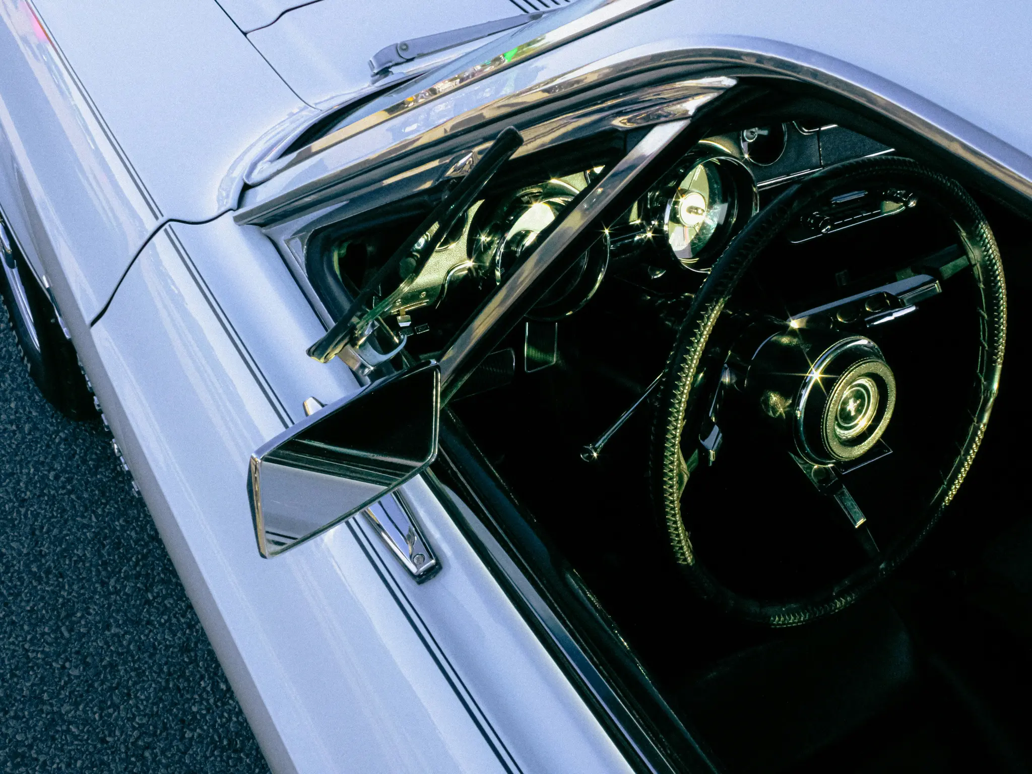 Detailní záběr z ptačí perspektivy na stranu řidiče bílého vintage vozu, zobrazující volant, palubní desku a boční zrcátko.