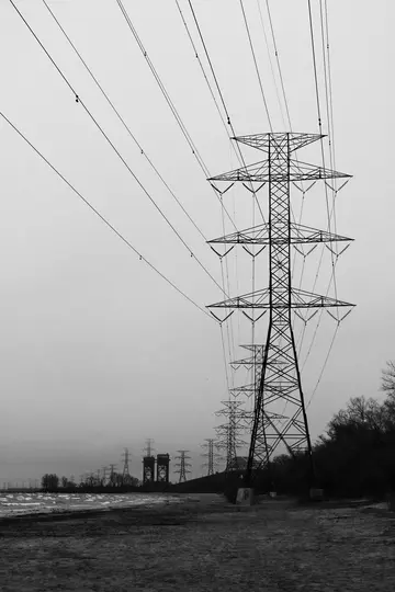 Et sort-hvidt billede viser en stor elmast i forgrunden, med en række lignende master der strækker sig ind i…