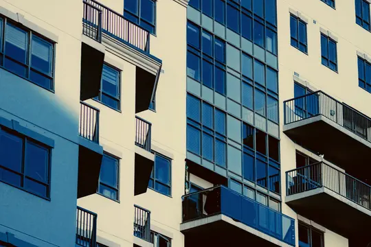 Una fachada moderna de edificio con paredes de color crema, ventanas tintadas de azul oscuro y balcones negros con