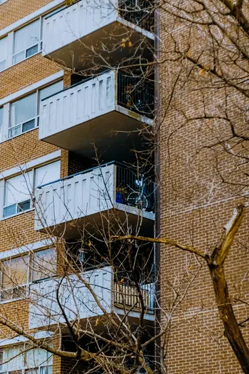Et nærbillede af en murstensbygning med flere hvide altaner. Bare trægrene er i forgrunden.