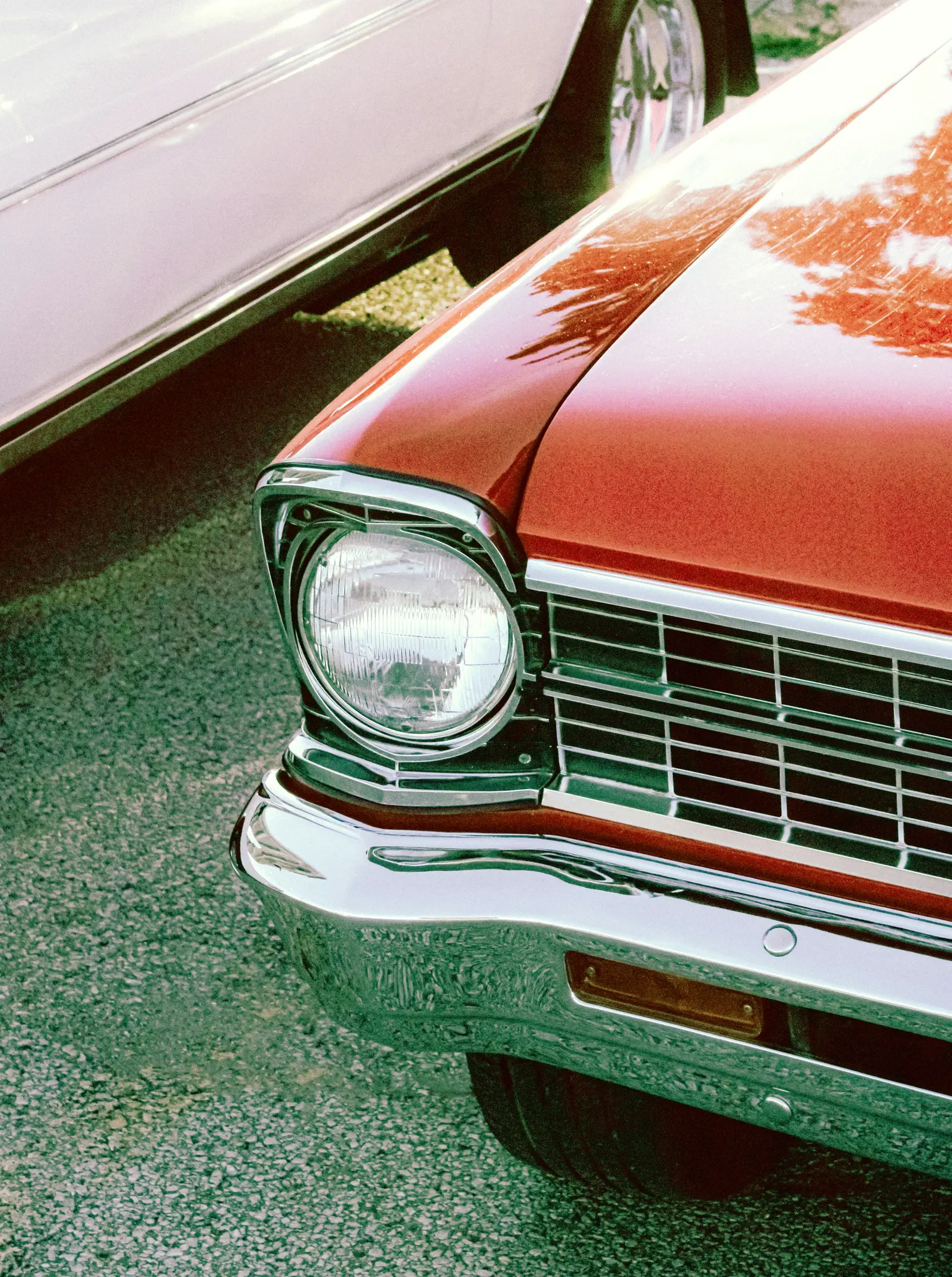 Un primo piano diagonale del lato anteriore destro di un'auto rossa vintage, con il suo faro rotondo, la griglia cromata e…