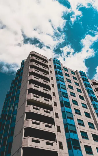Una toma en ángulo bajo de un edificio alto y de color claro con muchos balcones y ventanas teñidas de azul brillante, contra