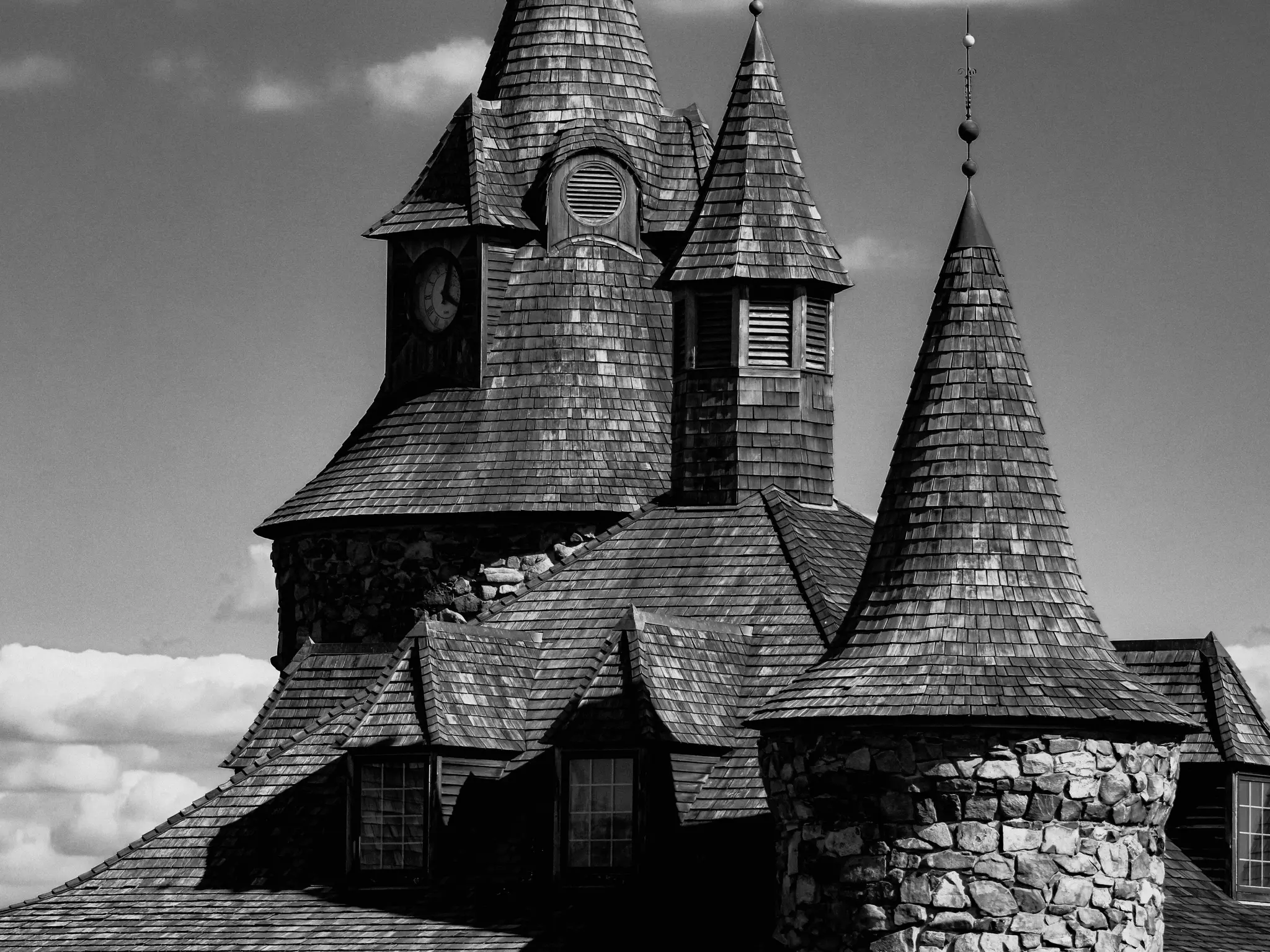 Černobílá fotografie zobrazující horní část budovy s několika kuželovitými věžičkami pokrytými dřevěnými šindeli. Kamenné...
