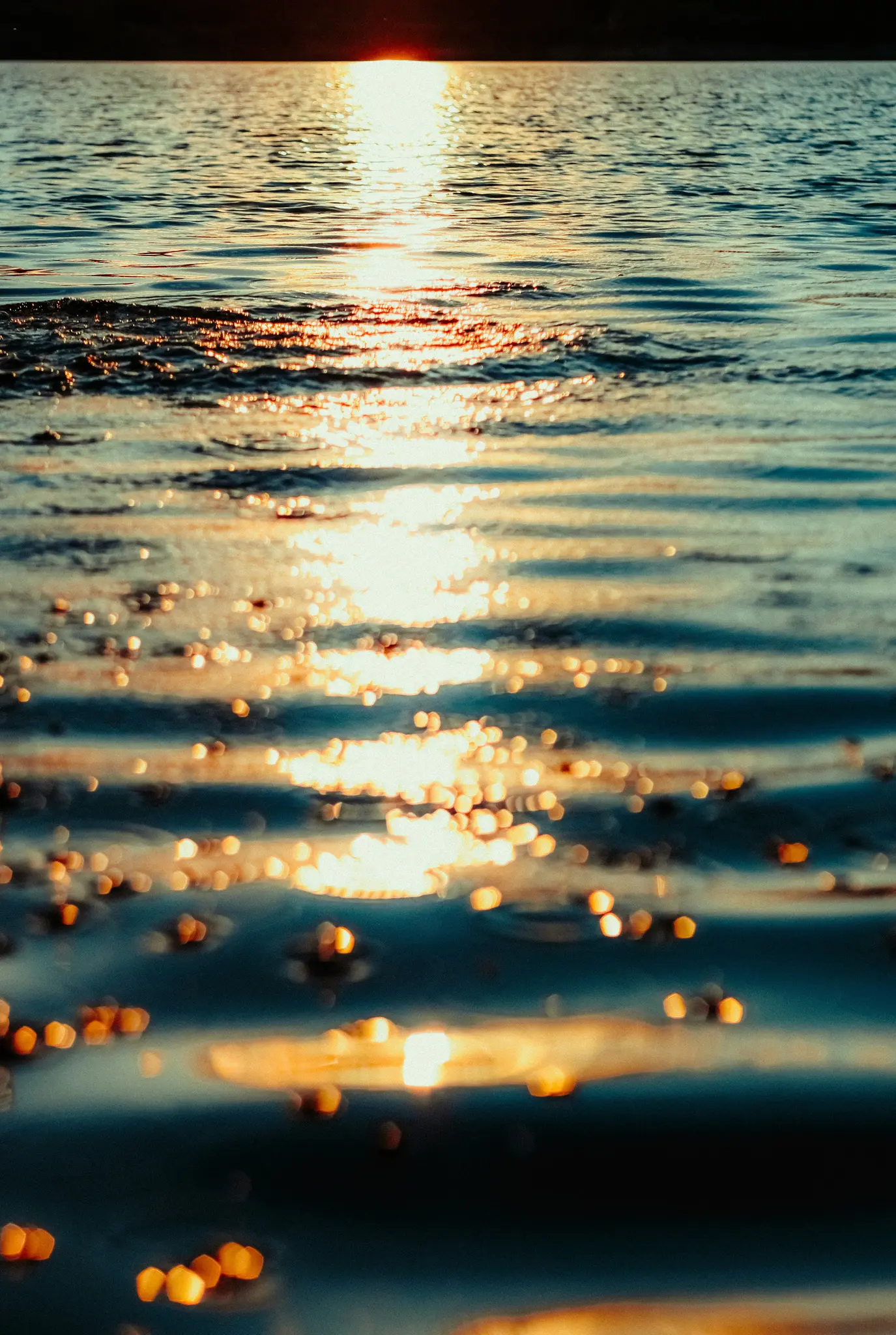 Un primo piano, scatto verticale di acqua con la luce dorata del sole che si riflette e scintilla sulla sua superficie