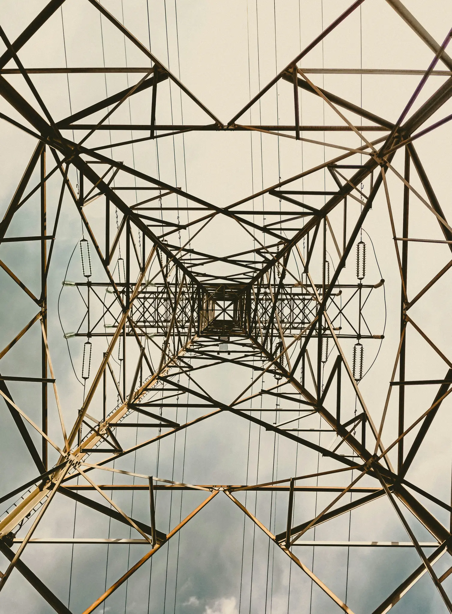 O vedere de jos în sus în complexul cadru metalic geometric al unui pilon electric mare pe un cer înnorat.