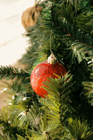 Nærbillede af et rødt, mønstret julepynt, der hænger fra en gren på et kunstigt juletræ.