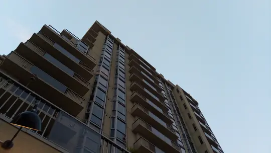 Et lavvinklet billede af en høj, moderne bygning med talrige altaner og reflekterende vinduer mod en lyseblå himmel.