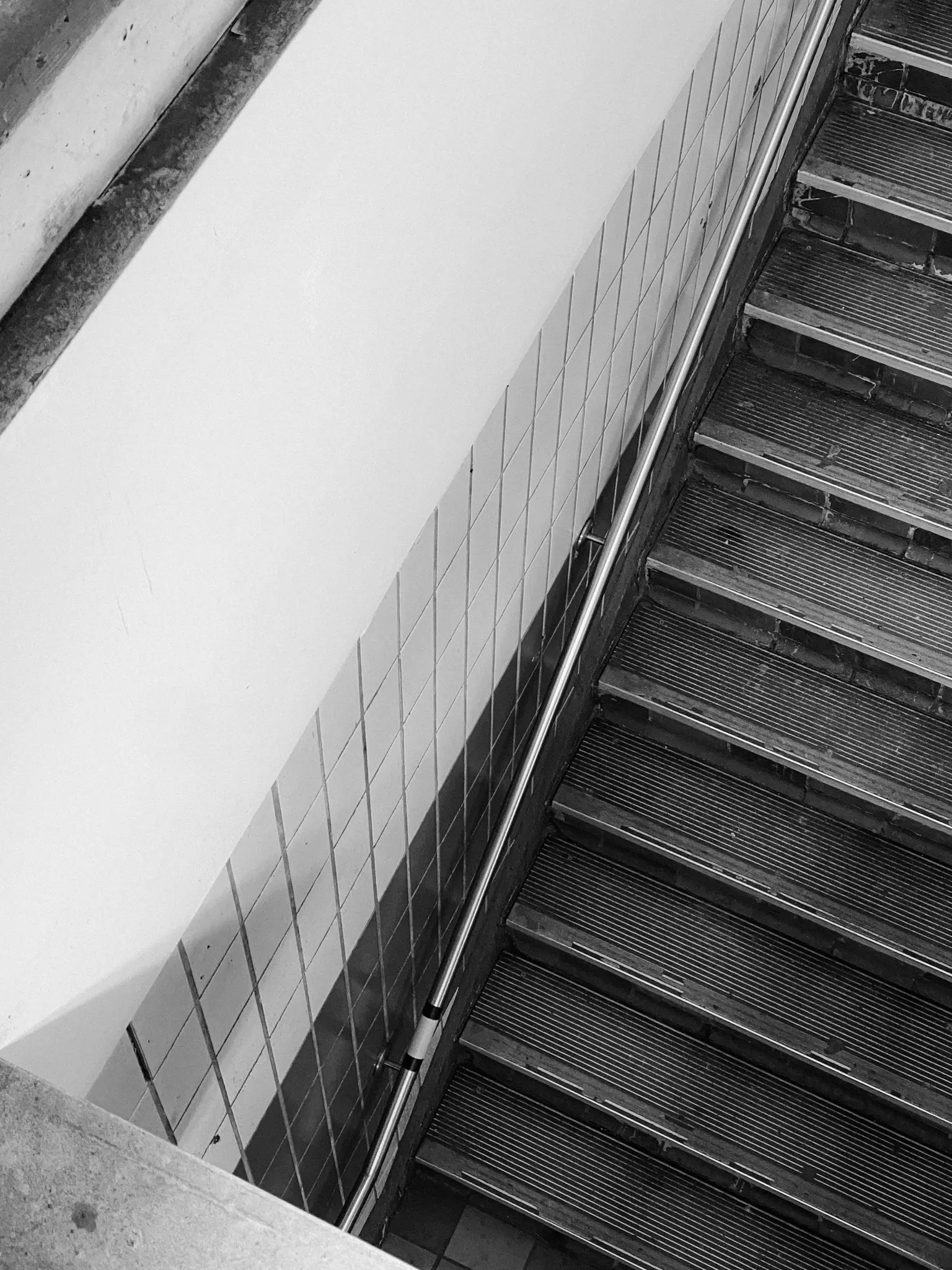 Una foto in bianco e nero, scattata dall'alto, di una scala con corrimano in metallo. La parete accanto alle scale è