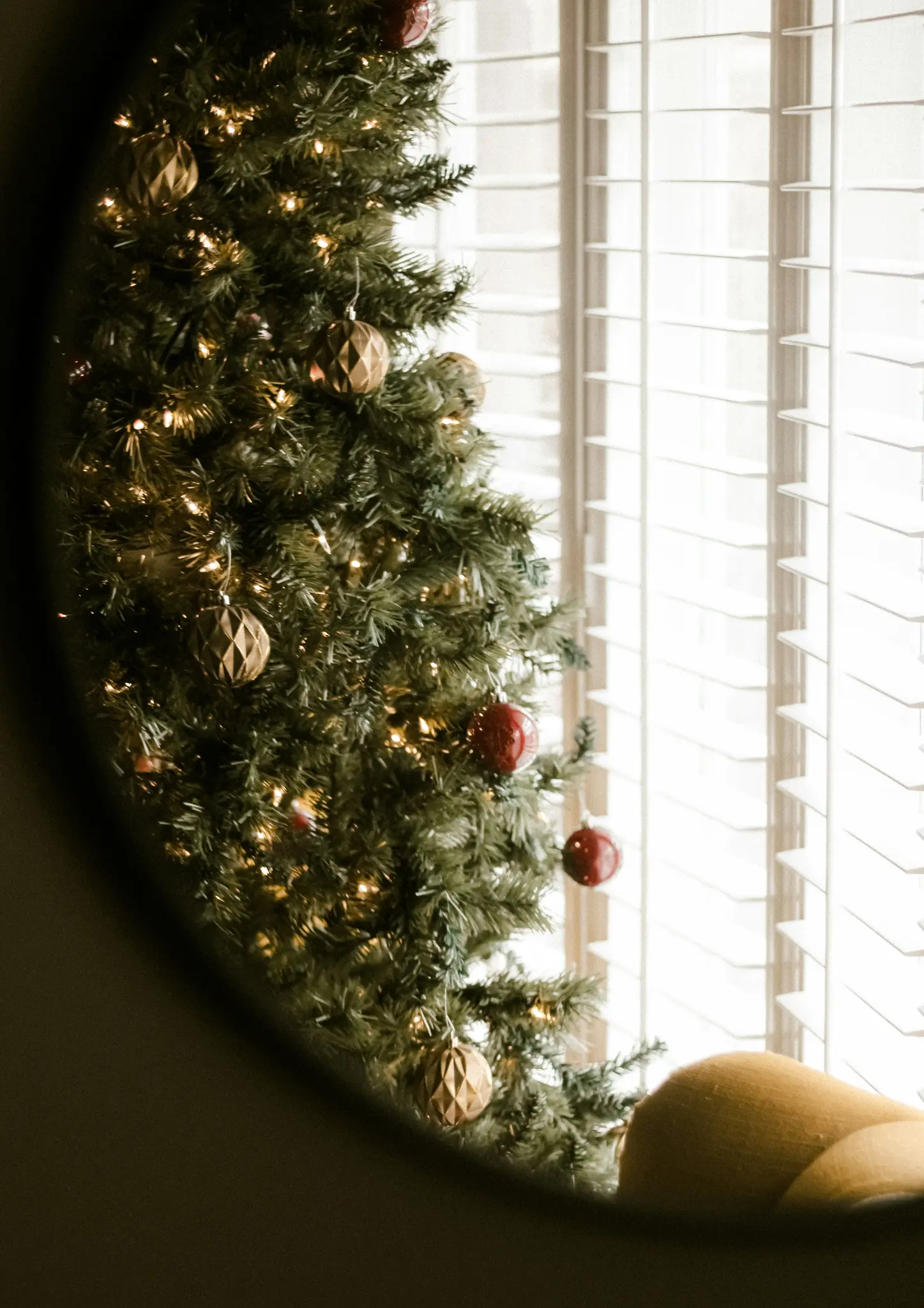 Un albero di Natale decorato con luci calde e ornamenti rossi e dorati è visto attraverso una cornice scura e curva, accanto