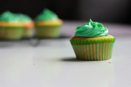 Et nærbillede af en cupcake med lys grøn hvirvlet glasur og gul kage i en grøn og gul stribet wrapper. To...
