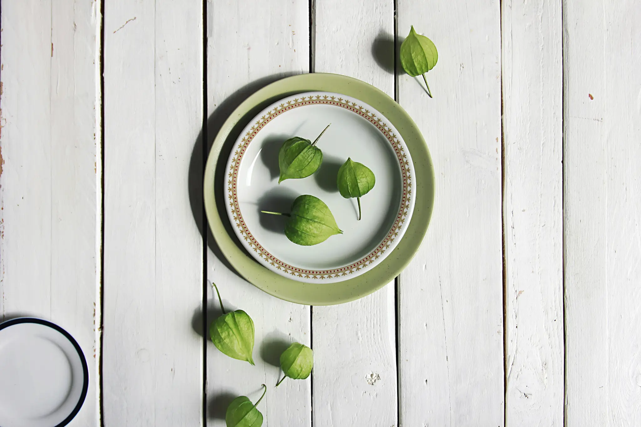 An overhead shot shows several green tomatillos, some on two stacked plates and others scattered on a white wooden surface.