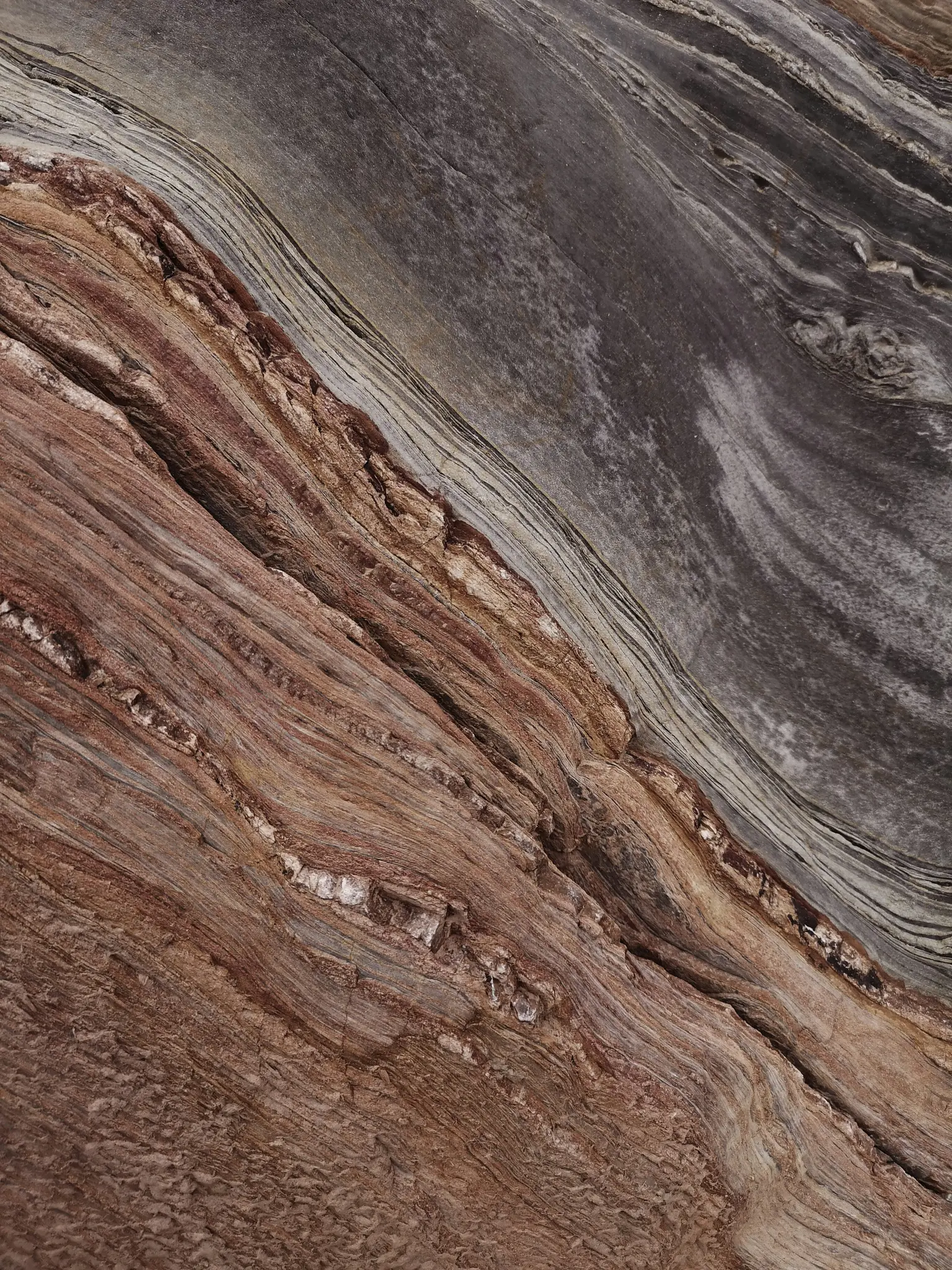 A close-up abstract image of a surface with diagonal lines and textures in shades of brown, red, and gray.