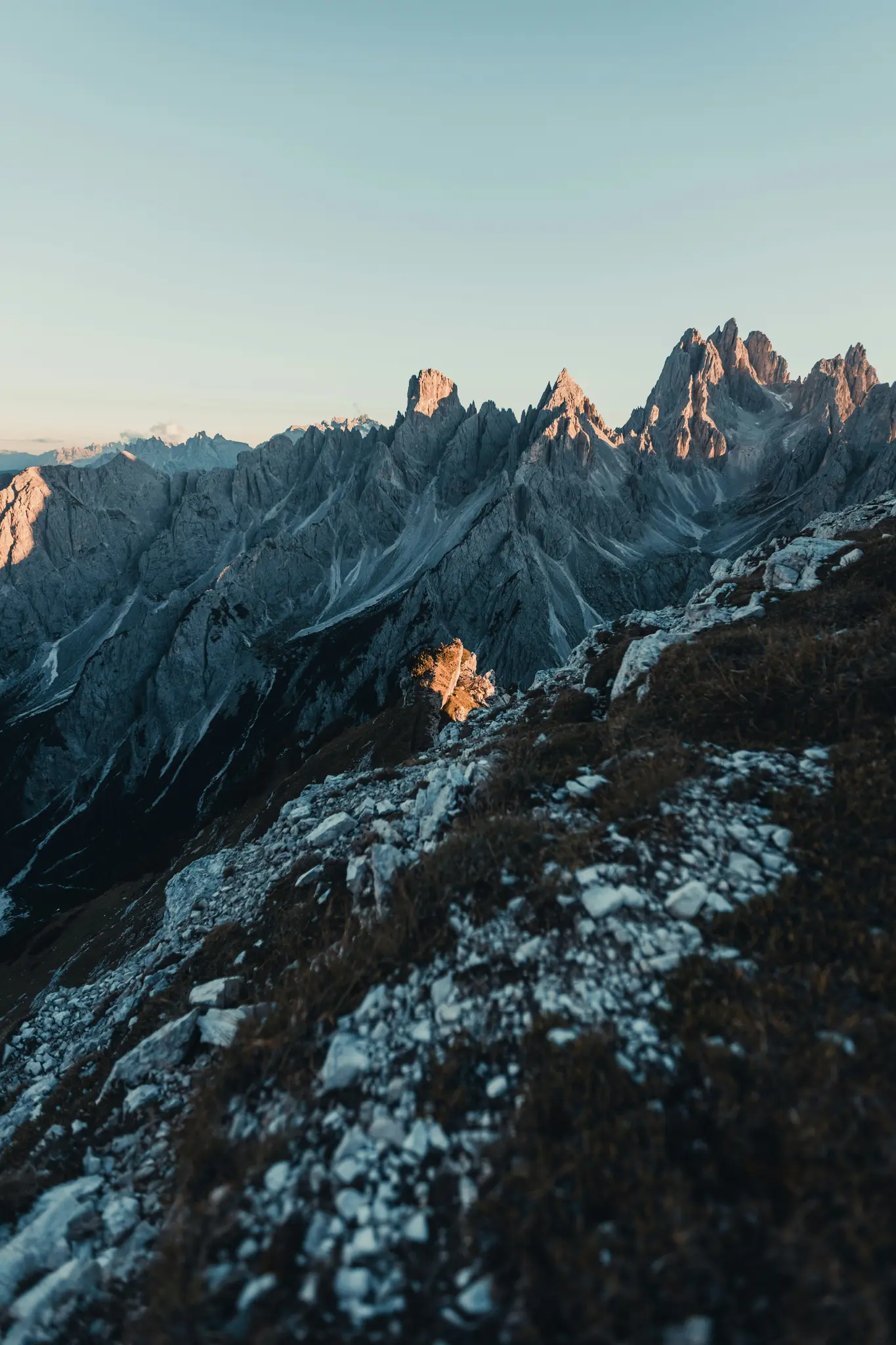 Ein atemberaubendes Landschaftsfoto, das raue, graue Berggipfel zeigt, die von goldenem Licht unter einem klaren blauen