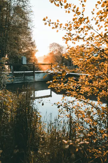 Ein hölzernes Schleusentor überspannt ein ruhiges Gewässer und spiegelt das warme Leuchten einer untergehenden Sonne wider.