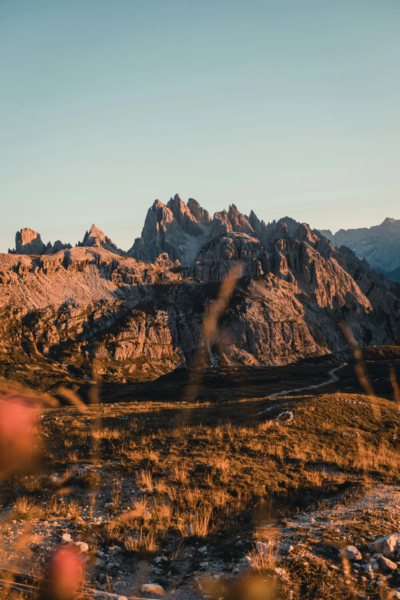Una foto de paisaje vertical que muestra una cordillera de montañas escarpadas y rocosas bañadas por la cálida luz dorada del