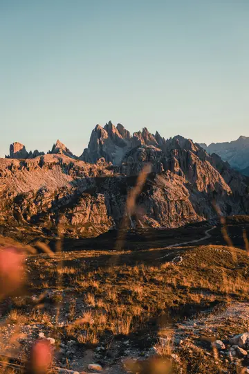 Ein vertikales Landschaftsfoto, das eine Reihe zerklüfteter, felsiger Berge zeigt, die im warmen, goldenen Licht des späten