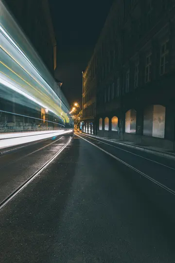 Ein Langzeitbelichtungsfoto einer Straßenbahn, die helle weiße und gelbe Lichtspuren erzeugt, während sie eine dunkle, nasse