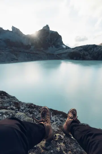 Eine Ansicht aus der Ich-Perspektive auf Wanderschuhe und Beine, die über eine felsige Klippe baumeln, mit einem leuchtend