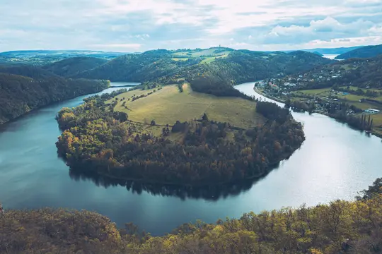 Una vista aérea muestra un río ancho haciendo una gran curva en S a través de un valle. Colinas cubiertas de árboles verdes y